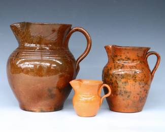 Three pieces of 20th century Jugtown Pottery.  Various forms, includes a Ben Owen pitcher with mottled Red/Brown Tobacco Spit glaze, a smaller pitcher with mottled Orange/Green Accidental glaze, and a creamer with Orange glaze.  Large pitcher with stamped "Ben Owen / Master Potter" mark, others with impressed "Jugtown Ware" marks.  Crazing, minor surface wear, a few edge flakes, creamer with painted underside.  3 1/4" to 8 3/4" high.  ESTIMATE $50-100
