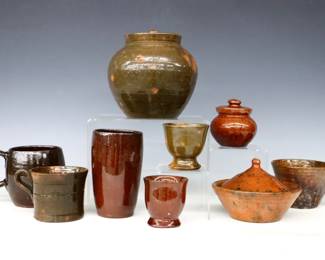 Nine pieces of 20th century Jugtown Pottery.  Various forms with mottled Red/Brown Tobacco Spit and Orange/Green Accidental glazes.  Includes a covered jar, a covered pot, three mugs, a tumbler, two toothpick holders and a small covered jar.  Impressed "Jugtown Ware" marks.  Some with crazing and flakes.  Up to 6" diameter and 6 1/4" high.  ESTIMATE $50-75