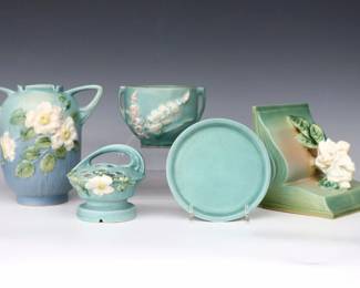 Five pieces of mid 20th century Roseville Art Pottery with Blue and Green matte glazes.  Includes an ovoid vase and flower frog and multi-color White Rose decoration, a single bookend with multi-color Gardenia decoration, a small planter with multi-color Foxglove decoration, and a simple saucer dish.  Molded "Roseville / U.S.A" marks and model numbers.  Minor wear.  Up to 7" diameter and 7" high.  ESTIMATE $50-100