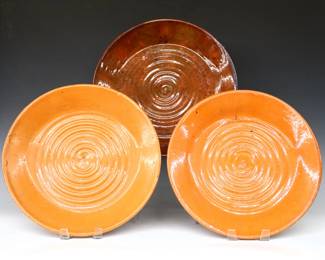 Three 20th century Jugtown Pottery pie dishes.  Circular forms with swirled decoration, includes two with mottled Orange glaze, and one by Ben Owen with Oxblood/Orange glaze.  Impressed "Jugtown Ware" marks, Oxblood platter with stamped "Ben Owen / Master Potter" mark.  Some crazing and flakes, Orange dishes with surface wear.  Up to 14 1/2" diameter.  ESTIMATE $50-100