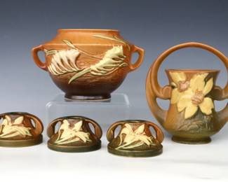 Five pieces of mid 20th century Roseville Art Pottery.  Includes an urn form vase with multi-color Freesia decoration and Orange/Brown matte glaze, a basket vase with multi-color Clematis decoration and Orange/Brown matte glaze, and three low candlesticks with multi-color Zephyr Lily decoration and Green/Orange matte glaze.  Molded "Roseville / U.S.A" marks and model numbers.  Minor wear.  Up to 7" diameter and 7" high.  ESTIMATE $50-100