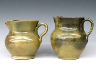 Two 20th century Jugtown Pottery pitchers.  Bulbous forms with ruffled rims, strap handles and incised decoration with mottled Green Frogskin glaze.  Impressed "Jugtown Ware" marks.  A few larger burst air bubbles from production, shorter with a couple small flakes, taller with short firing crack in handle.  6" and 6 1/2" high.  ESTIMATE $50-75