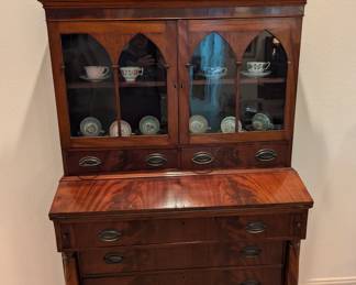 Gothic Revival Flame Mahogany veneer secretary bookcase, CA. 1860; the upper section with scrolled cornice flanked by urn finials above two arched fretwork paned doors over two short drawers above a fold-out slant-front desk over three graduated drawers.