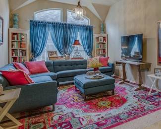 Living Room -Chandelier, blue curtains for 2 windows, L shaped sofa with large ottoman, console table, rug, and two corner bookshelves (part of a wall unit)