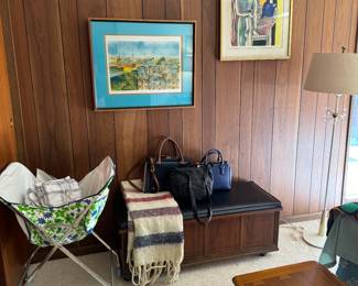 On the left is by Claude Grosperrin, French signed lithograph of Paris rooftops. On the right is a French Fernand Leger watercolor, “Woman in Green Dress”. Vintage cedar chest and bench by Lane.
