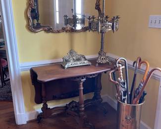 These pieces are in the entrance hall. Walnut Tea/Game table, brass ink well, English brass umbrella stand, brass candelabra and wonderful gold leaf carved frame mirror with painted top panel