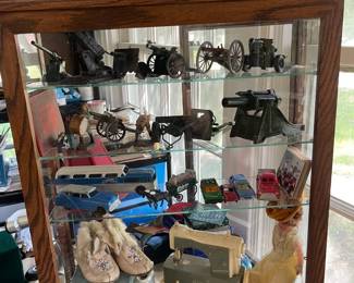 This showcase contains model canons, vintage cars, baby shoes, vintage toy sewing machine, doll tea set and more stamps. Iron Scottie Dogs and bronzed baby shoes
