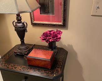 Black side table with hand-painted details, drawer and lower shelf, framed print, lamp, bud vase and wood box