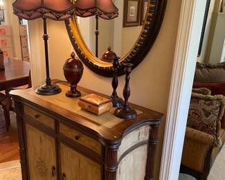Entryway console cabinet with 2 drawers and lower cabinet, oval mirror (black and gold), metal taper candle holders, urn, music box, and lamp