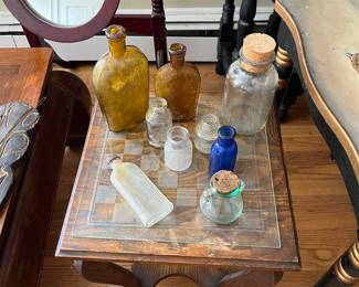 Assorted glass bottles on a low wood table with a glass checkerboard 
