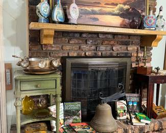 Notice the Jim Bean whiskey decanters on the mantle by the vintage sea scape. On the hearth is a vintage small table with a brass punch bowl set on it.  Surrounded by vintage gardening books is a magnificent large brass bell.
