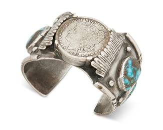 376
A Southwest Navajo Silver Coin Cuff Bracelet
Mid/late 20th century, Diné
Stamped: KEE [with serif]
A heavy gauge silver watch cuff with four large turquoise stones in handmade bezels and topped with an 1897 Morgan silver dollar piece
7" inner C x 2" H, with a 1.25" gap
168.8 grams gross
Estimate: $700 - $900