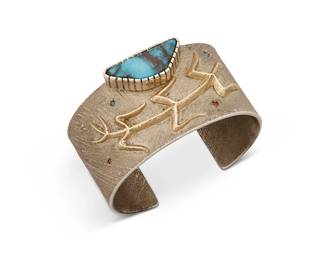 380
A Southwest Silver And Gold Cuff Bracelet
Late 20th century
Stamped plaque: [partially obscured] Redhorse / Alvarez
A sandcast silver cuff with applied gold corn stalk and off-set turquoise stone and seven scattered faceted stones throughout
7" inner C x 1.5" H, with a 1.25" gap
114.6 grams gross
Estimate: $500 - $700