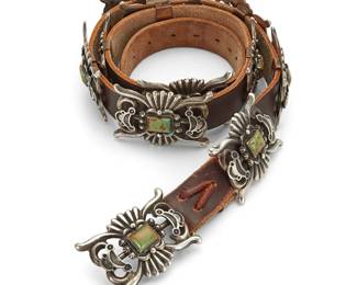 438
A Randall Joe Tom Navajo Sterling Silver And Turquoise Concho Belt
Randall Joe Tom (b. 20th century, Diné)
Late 20th century
Buckle stamped: R. Tom / Sterling
A narrow heavy belt with an ornate openwork concho buckle with heavily stamped applied silver accents and set rectangular green turquoise stone with ten matching rectangular conchos, and all mounted to a brown leather strap
Buckle and each concho: 1.75" H x 2.5" W; belt: 40" L x 1" H
541.3 grams gross
Estimate: $800 - $1,200