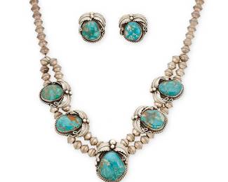 367
A Set Of Southwest Sterling Silver And Turquoise Jewelry
Mid/late 20th century
Stamped: _J [obscured] / Sterling
Comprising a squash blossom necklace with central turquoise-set blossom and drop with applied silver feather motifs and four further blossoms, all fixed to silver beads, together with a pair of matching pierced earrings, 3 pieces
Necklace: 20" L x 2.5" H; each earring: 1" H
100.2 grams gross
Estimate: $500 - $700