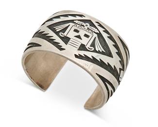 407
A T. Thomas Navajo Sterling Silver Cuff Bracelet
Late 20th century, Diné
Stamped: T. Thomas / Sterling; further stamped: [sun] / LA [conjoined]
A chunky cuff silver overlay cuff with masked Hopi figure set in a serrated lozenge
6.5" inner C x 1.5" H, with a 1.125" gap
109.6 grams
Estimate: $300 - $500