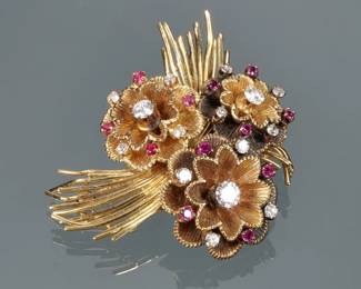 RUBY, DIAMOND, & 18K GOLD FLOWER FORM PIN EN TREMBLANT | Designed as three free-spinning 18k gold flower heads mounting round brilliant diamonds and small round mixed cut rubies, supported on an 18k wirework backing, double pins marked with "750" and an unusual makers mark with a planet (saturn), star, and "LL"; 2 in., 26.8g

