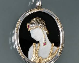 ERTE RUBY, DIAMOND, GOLD & STERLING PIN | Art Deco Salome brooch/pendant designed as a mother of pearl bust adorned in 14k gold garments set with two rubies and graduated diamonds, set in a sterling silver surround, marked on the back "CFA 14K & S/S"; 24.68g - w. 1.75 x h. 2 in. (without bail)