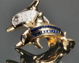 SAPPHIRE, DIAMOND, & 14K GOLD DOLPHIN PIN | Designed as two dolphins, one diamond-encrusted, the other having two rows of square cut sapphires, each with a sapphire cabochon eye, all set in 14k yellow gold, with fineness mark on the back; 2 in., 13.5g

