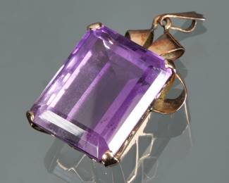 A LARGE RECTANGULAR CUT AMETHYST & 14K GOLD PENDANT | Designed as a central rectangular mixed cut, amethyst (20 x 15.7 x 10.8 mm) set in a (tested to) 14k gold ribbon form surround; 1 in., 9.0g.

