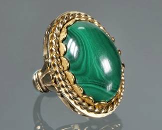 MALACHITE CABOCHON & 14K GOLD RING | Designed as a central solid polished oval malachite (20.5 x 15 x 8.1mm) set in a 14k yellow gold twisted rope border and with an open scrollwork gallery; size 3, 15.4g; marked "585".

