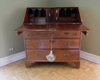 Antique slant front desk, top opened as writing surface, resting on supports; showing interior drawers, cubby holes, and additional locked compartment