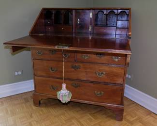 Another view of antique slant front desk, top opened as writing surface, resting on supports; showing interior drawers, cubby holes, and additional locked compartment