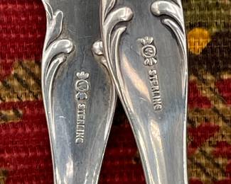 Close up of sterling silver and silver plate serving spoons, teaspoons, sugar tongs, salad serving set
