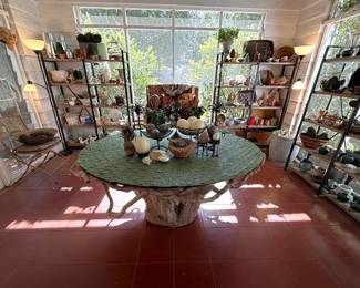 Screened porch filled with curiosities. There are baskets from around the world, textiles from Africa, porcelains, masks and an amazing tree trunk table cut from a tree on the property many years ago.