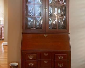 Jasper Cabinet Company Colonial Cherry secretary with a slant top, a four-drawer block front, crown (“wavy”) glass doors, and solid brass hardware. One-piece.
Features built-in light, multiple storage compartments, and antique black leather inlay writing surface.
Adjustable glass shelves include plate rail.
Measures 35”W × 18”D× 84ʺH, moulding detail at top and bottom adds approx. 1” to width and depth.