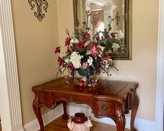 Ornate carved writing desk w/claw feet, large framed mirror, floral arrangement. pottery vase