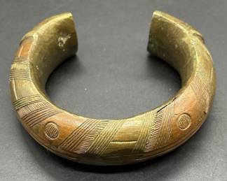Antique African Engraved Brass Currency Bracelet. This piece, along with several other African artifacts comes from an estate in the Atlanta, GA area. We do not know anything about its origin as it was found behind hidden within the walls of an old home that was being torn down. The bracelet has intricate engravings as shown and it is a very heavy piece weighing in at 15 Oz. It is approx 3.5” in diameter and it is a approx 1.25” thick at its thickest point as shown.