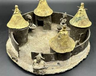 Bronze African Village Diorama Sculpture Found In Old House In Atlanta, Georgia. This primitive sculpture is one of two, along with other African artifacts, found behind an inside wall of an old home in Atlanta, Georgia while it was being torn down. The origins and creator of the sculpture are unknown. The sculpture/diorama features a tribal village scene with four huts surrounded by a wall. A watchful tribesman is standing outside the village entrance while a sleeping dog lays on the opposite side of the entrance. Inside, two village women prepare food in large pots while a cat slinks around the perimeter of the wall. There are four huts with removable bronze roofs. One of the tribal women has broken arms, one of which is present. Beyond that, the set is well preserved overall. The sculpture diameter is approximately 9 inches and the weight is 2 lbs