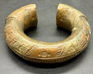 Antique African Engraved Brass Currency Bracelet. This piece, along with several other African artifacts comes from an estate in the Atlanta, GA area. We do not know anything about its origin as it was found behind hidden within the walls of an old home that was being torn down. The bracelet has intricate engravings as shown and it is a very heavy piece weighing in at 1Lb 8oz. It is approx 3.75” in diameter and it is a approx 1.5” thick at its thickest point as shown.