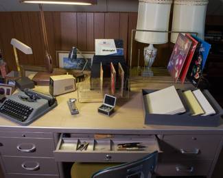 Another view of metal desk, typewriter, desk lamp, filing materials