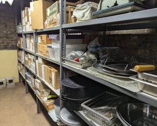 Basement racks filled with catering kitchen ware - large stainless steel mixing bowls, lidded graniteware roasting pans, trays, stock pots