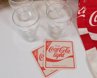 Closeup of Coca Cola brand merchandise including plastic cooler, shorts, pants, glasses, coasters, bottle crate