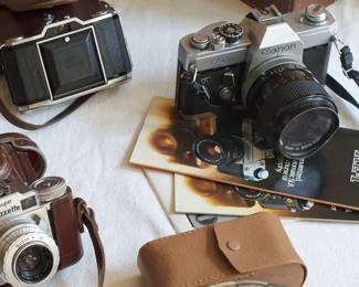 Closeup of vintage cameras and leather cases including Paxette, Agfa, Bell & Howell, Canon, and Zeiss Ikon
