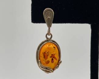 Closeup of pair of amber earrings, amber held in oval decorative metal frame, inclusions visible suspended in the amber
