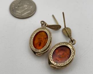 Closeup of pair of amber earrings, amber held in oval decorative metal frame, inclusions visible suspended in the amber