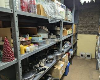 Basement racks filled with catering kitchen ware - lidded saucepans, frying pans, measuring cups, cake pans, pot rack; some holiday decorations