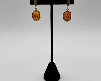 Pair of amber earrings, amber held in oval decorative metal frame, inclusions visible suspended in the amber