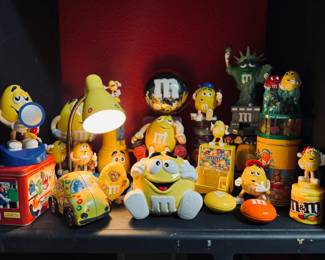 The ultimate collection of M&M's memorabilia highlights the playful and collectible nature of M&M's merchandise, including various figurines, tins, and novelty items like a Statue of Liberty-themed piece and a yellow car.