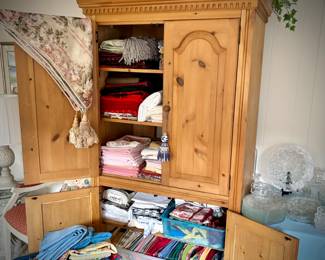 Pine armoire filled with linens (tablecloths, runners, napkins, and placemats) and fabric remnants