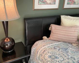 Another view of the leather headboard, side table, lamp  and a few of the linens and framed prints above bed