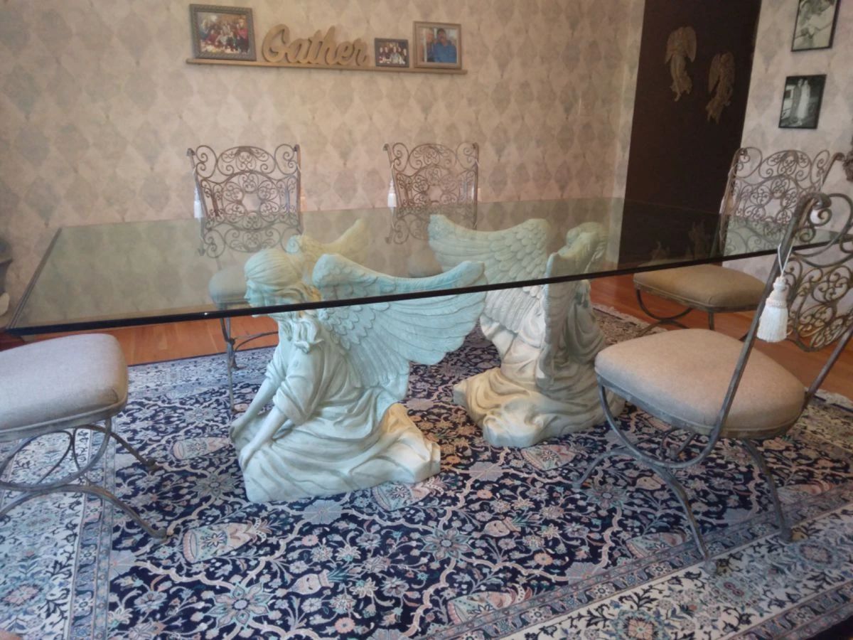 Unique FUNCTIONAL ART! This is a custom made, one-of-a-kind gorgeous Angelic Dining Table. Twin angels kneel quietly under this unique and original glass top table. Sculpted with the utmost care and attention to detail. Featuring intricate details on their wings and hair. Lavishly clothed in flowing gowns. Elegant triple waterfall edge finish on boat shaped ¾” thick glass top. Seats up to 12 people. Base 29” Tall. Wingspan 36” Glass top 4’ X 8’. Includes 12 wrought iron dining room chairs finished in a light bronze and cream colored cloth seats. Beautiful scrolls and details on chair back. A beautiful and unique dining room table to bring a little heaven to your family gatherings. Includes original architectural drawings signed by the artist. If you want a table NO ONE else in the world has, this one is for YOU!