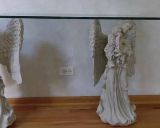 Angel Sofa Table Twin angels with cherub create this unique sofa table. Very unique and beautiful. Gorgeous feather details exquisite facial features on mother and cherub. Fiberglass/resin. Antique Stone. Elegant triple waterfall edge finish on rectangle ½” thick glass top. Base 28” Tall. Glass top measures 14” X 48”.