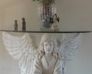 One of a kind Angel Entry Table. Beautiful angel kneels quietly under this unique and original glass top table. Sculpted with the utmost care and attention to detail, she is serene and lovely. Featuring intricate details on her wings and hair. Lavishly clothed in a flowing gown. Produced using the highest quality fiberglass/resin for strength and durability. Ogee edge finish on half oval shaped ½” thick glass top. Base 29” Tall. Wingspan 36” Glass top 42”L 30”D.