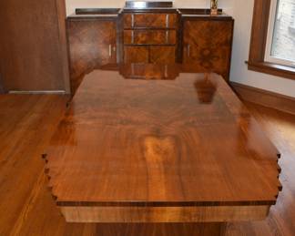View of two pieces from the stunning 1930s Art Deco dining room set - The stepped edges on the table and sideboard are quintessential Art Deco, invoking a sense of balance and harmony while maintaining a striking, modernist aesthetic. The rich, figured burl wood, likely walnut or mahogany, is finished with a high-gloss lacquer that amplifies the intricate natural patterns of the wood.