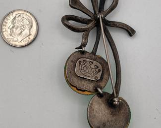 Reverse of Maria Loran green glass cherry brooch with rhinestones, brushed metal frame, green rhinestone bow tied at top of the cherry stems. The pin is stamped on the back Loran in a crown. 